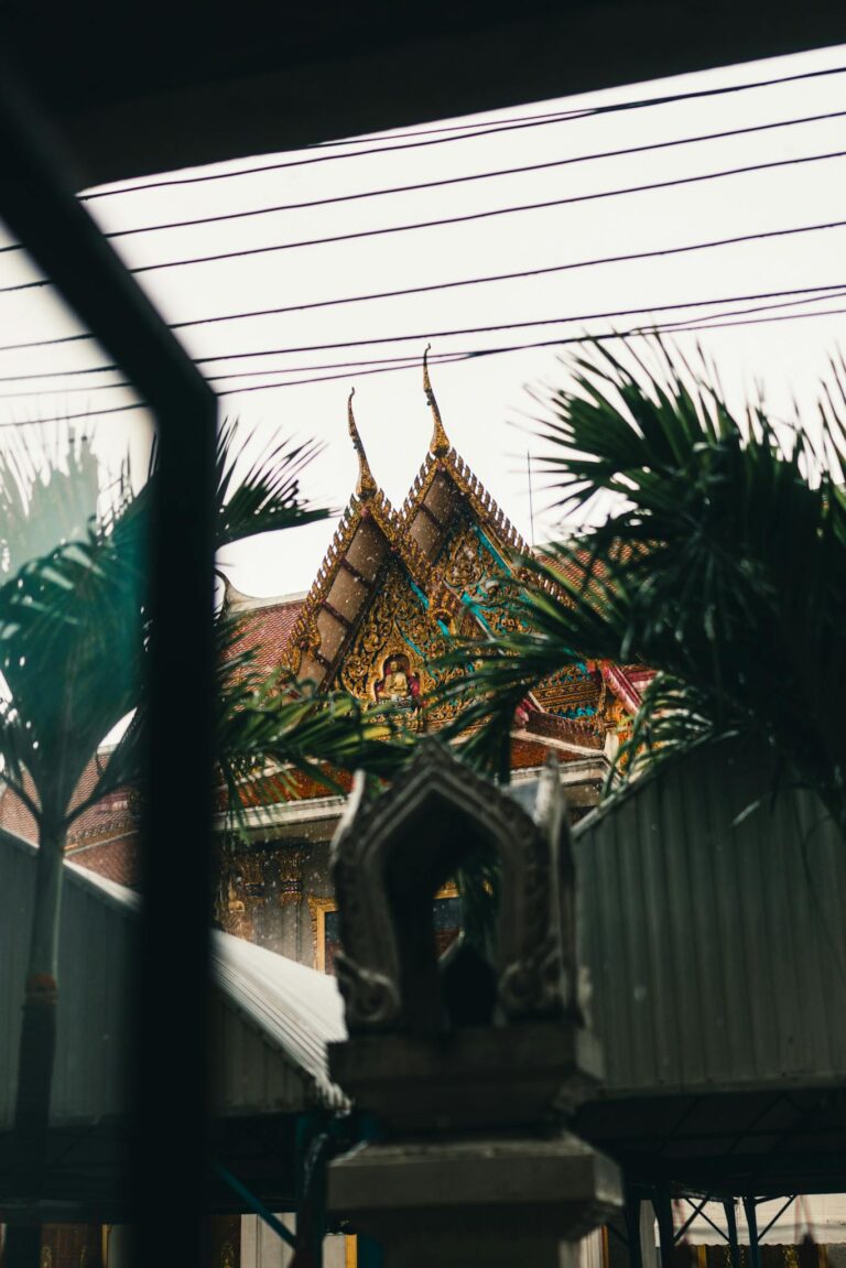 A glimpse of a traditional Thai temple in Bangkok through a window with palm trees in view.