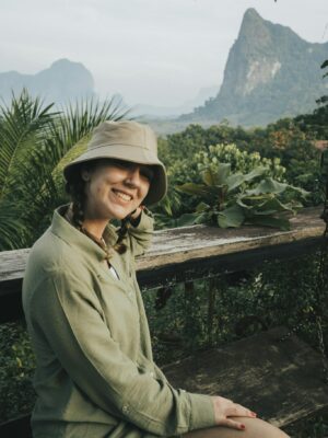 Smiling woman with hat sitting in lush tropical Krabi landscape.