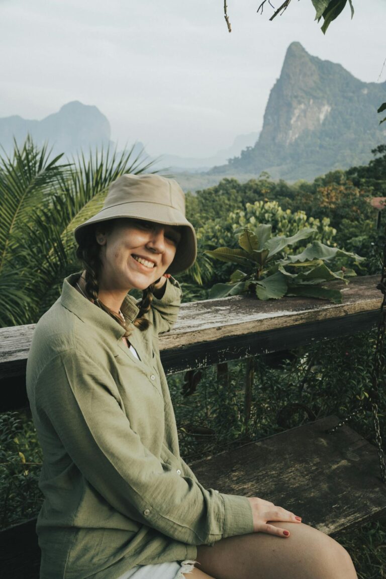 Smiling woman with hat sitting in lush tropical Krabi landscape.